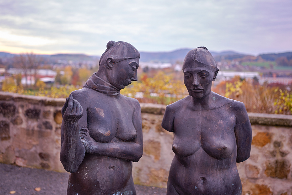 Auch in Burgkunstadt neben der alten Vogtei stehen einige Figuren von Uhlig. Hinter diesen beiden Frauen mit dem Titel "Verkündigung" öffnet sich der Blick über das Maintal bis zum Kordigast. Die Steinfigur links stammt von Manfred Reinharts "Fließende Begegnung" und steht bei Wiesen am Mainradweg. Die Lauter fließt in den Main - wobei die weibliche Figur für den Bad Staffelsteiner Nebenfluss steht.